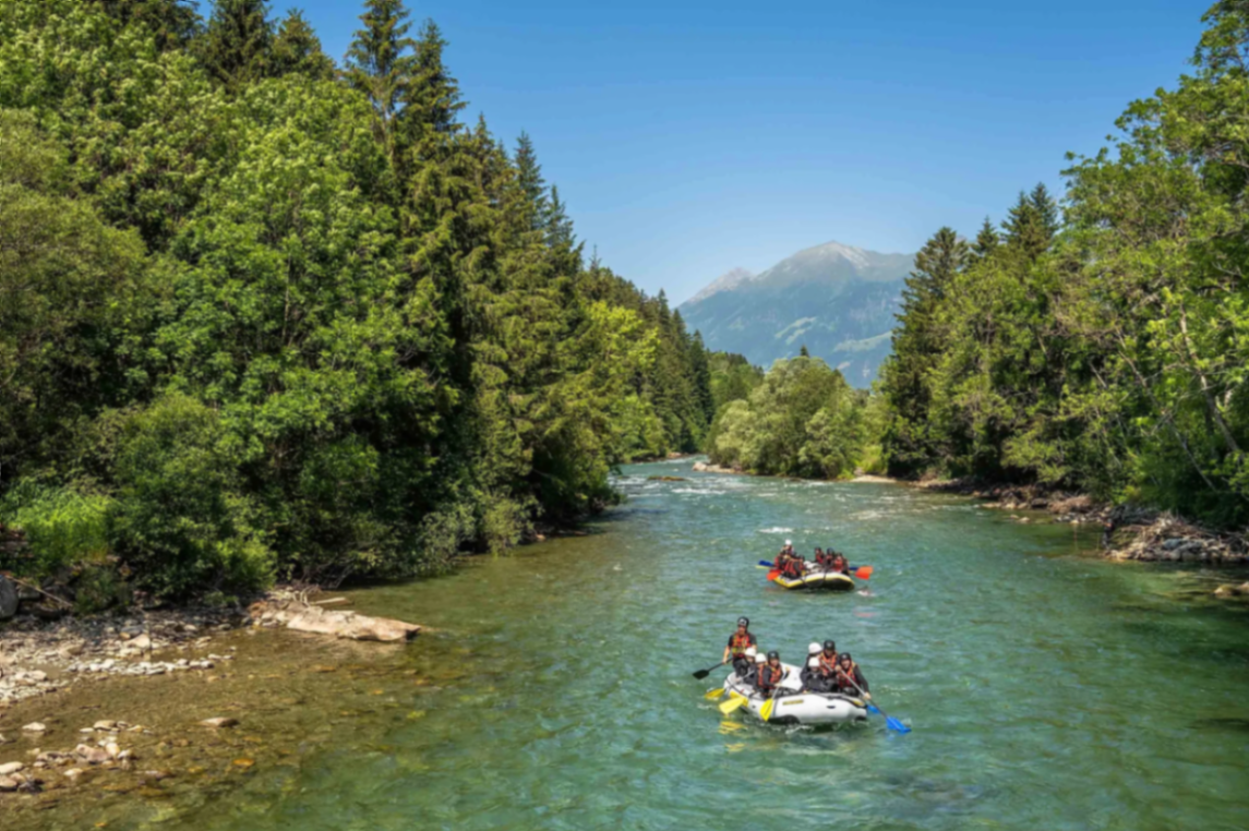 Zwei Rafting-Boote auf einem ruhigen Bergfluss zwischen Wäldern