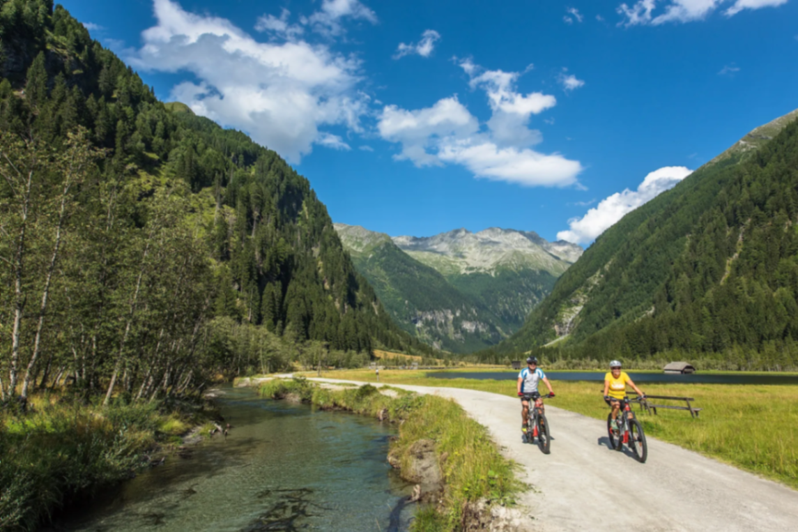 Radfahrer auf Schotterweg entlang eines Bergbachs im Tal