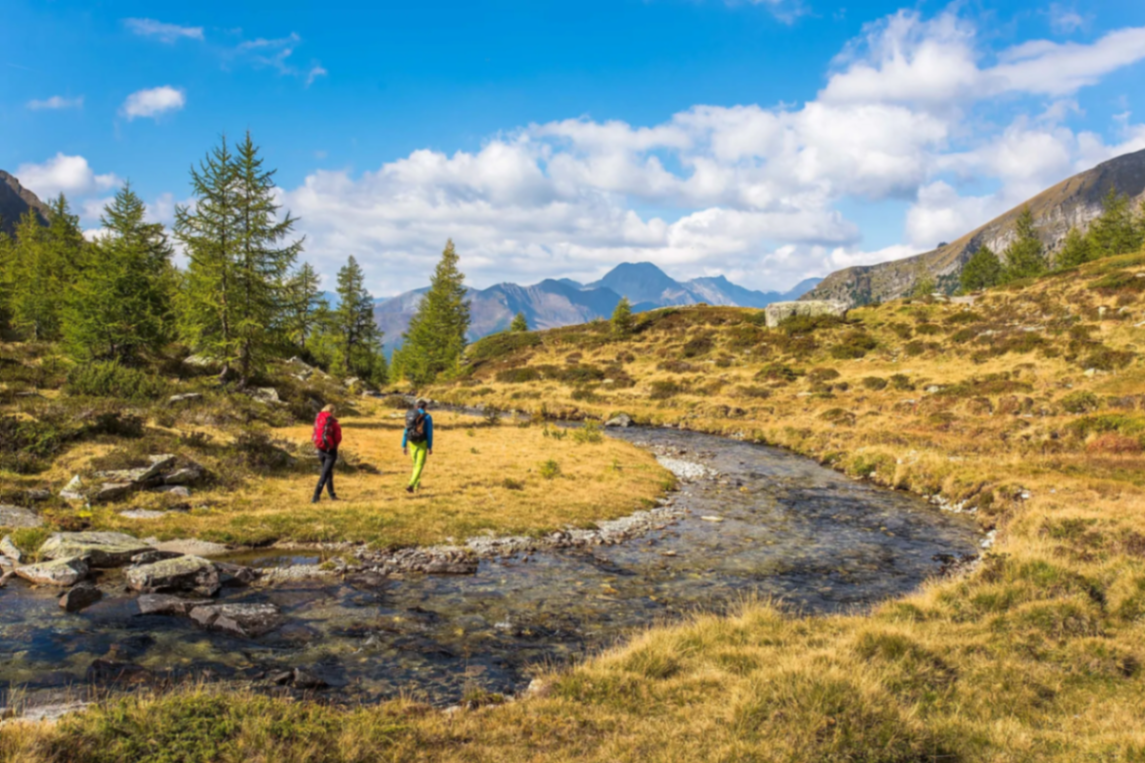 Zwei Wanderer am Gebirgsbach mit Bergpanorama